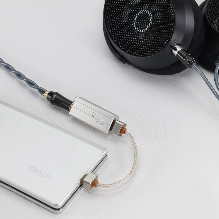 ddHiFi TC44Pro E3 DAC dongle attached to device and over-ear headphones sitting on white table