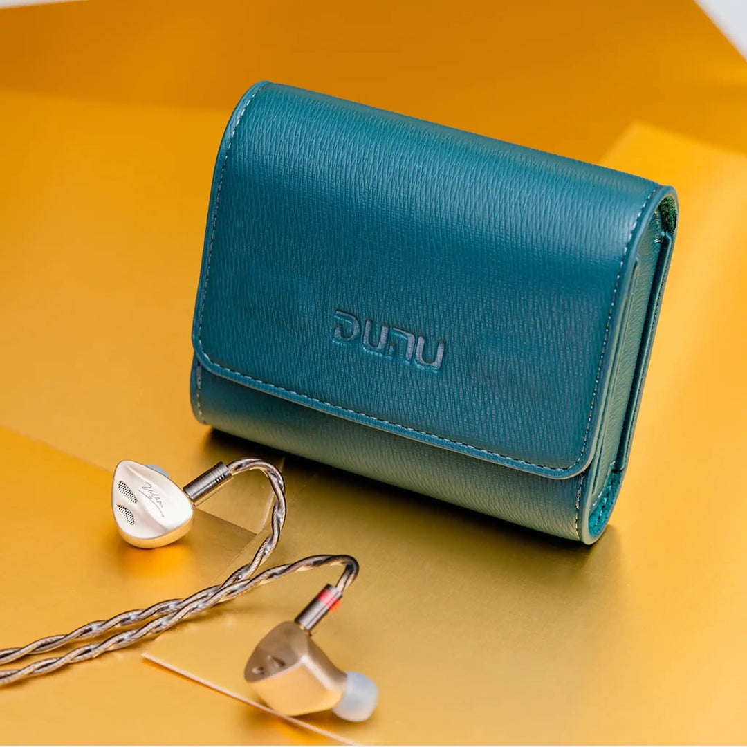 DUNU Vulkan IEMs sitting with cable attached with blue carrying case on gold paper sheets on the ground