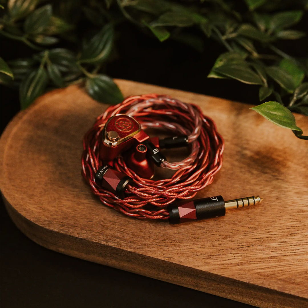 Eletech x Bloom Crimson IEM cable coiled with 64 Audio U18t IEMs sitting on wooden plant with plant on black table