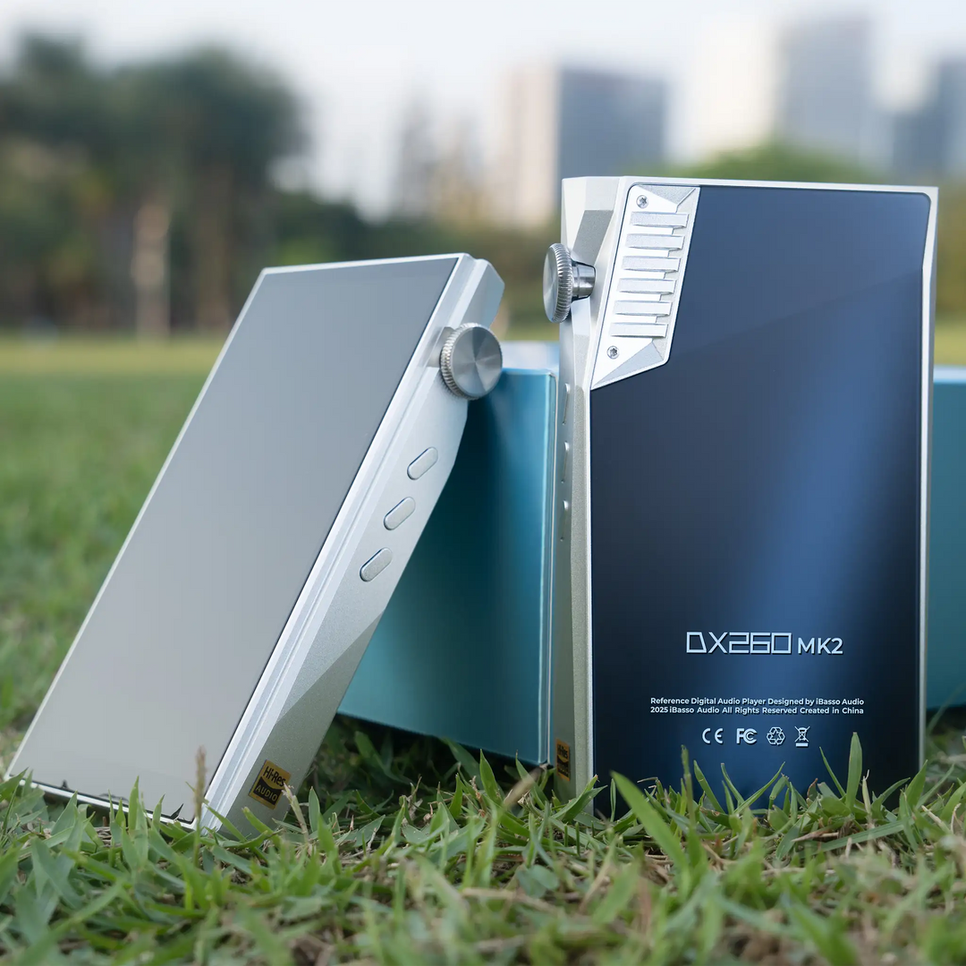 iBasso DX260MK2 DAP in silver and white silver standing in front of product box in grass with city background
