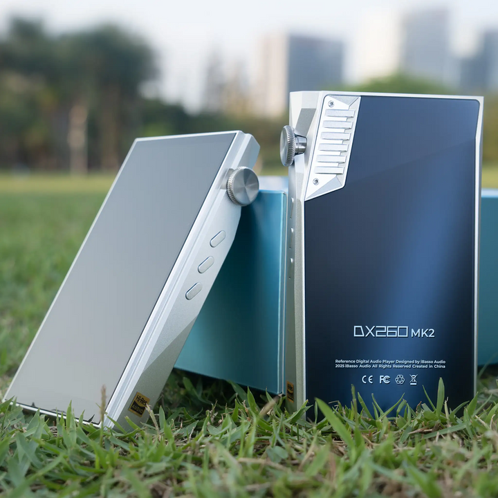 iBasso DX260MK2 DAP in silver and white silver standing in front of product box in grass with city background