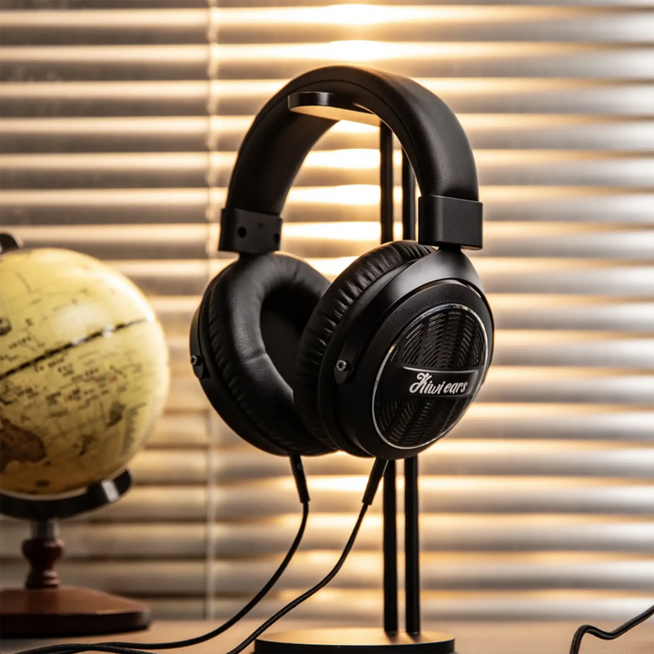 Kiwi Ears Ellipse headphone sitting on black headphone stand on table with globe