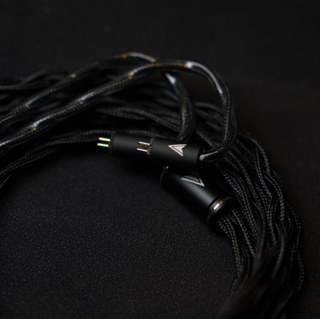 Astral Acoustics Voyager OFC Black braided iem cable with metallic connector housings and small colored pin accents, photographed on a dark textured background.