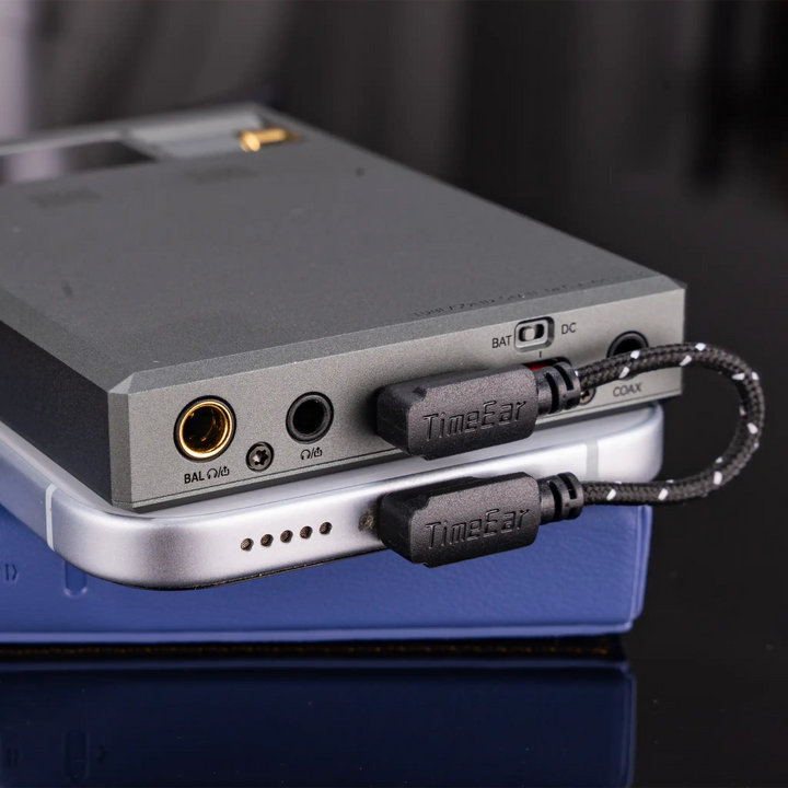 Cayin RU9 DAC and amp lying on top of leather case and smartphone showing magnetic back panel and L-shaped USB cable