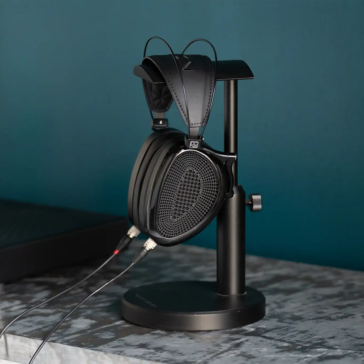 Dan Clark Audio Noire XO headphones sitting on black headphone stand right side view with blue wall behind