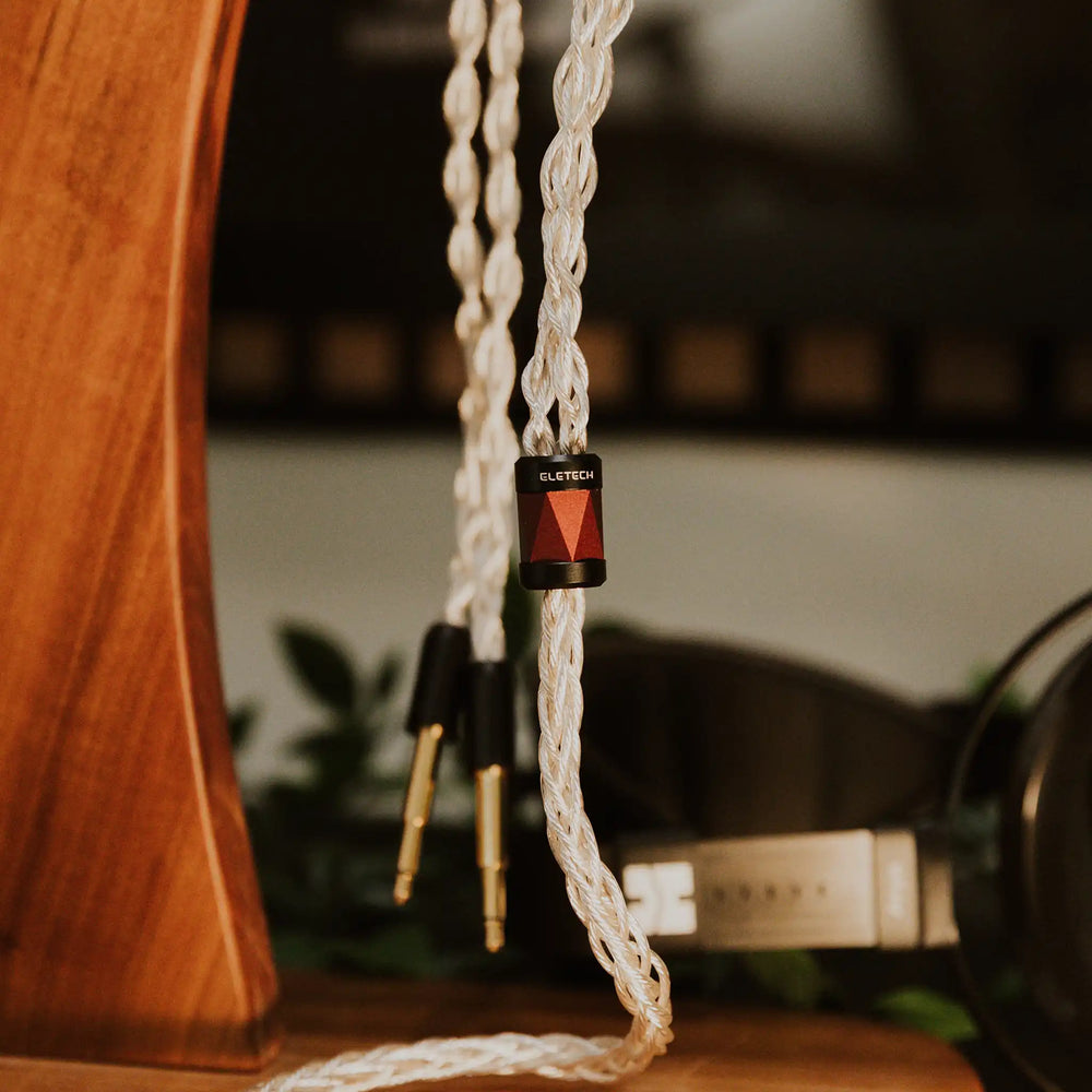 Eletech x Bloom Sage headphone cable hanging on wooden headphone stand y-split in focus with HIFIMAN Arya Unveiled behind