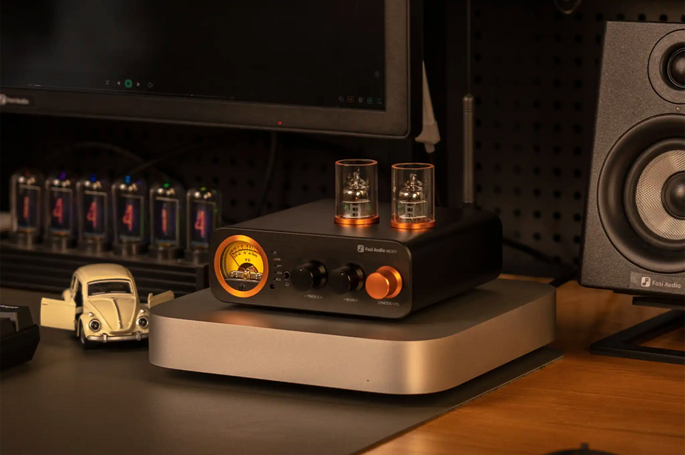 Fosi Audio MC331 DAC/amp sitting front right 3 quarter angle on silver platform on wooden desk with monitor and speaker