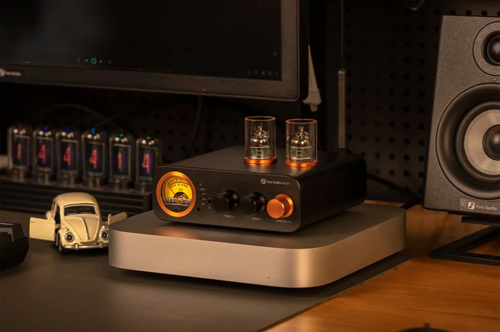 Fosi Audio MC331 DAC/amp sitting front right 3 quarter angle on silver platform on wooden desk with monitor and speaker
