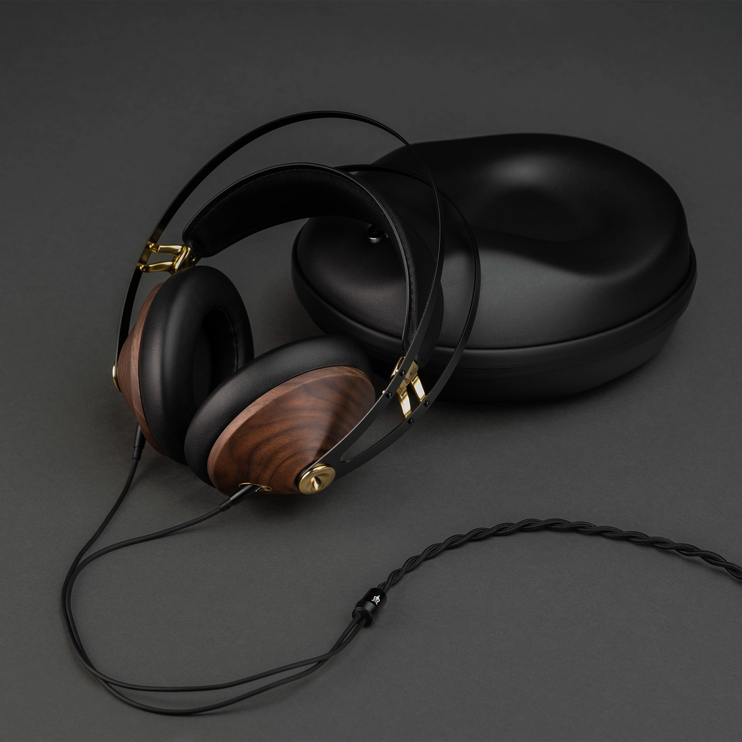 Meze 99 Classics 2nd Gen headphones leaning on hard shell case sitting on grey background with cable attached