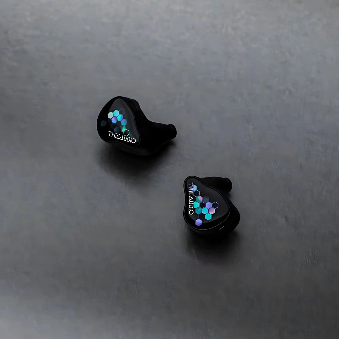 Thieaudio Monarch MKIV IEMs with Kaleidoglow faceplate sitting diagonally face up on grey background