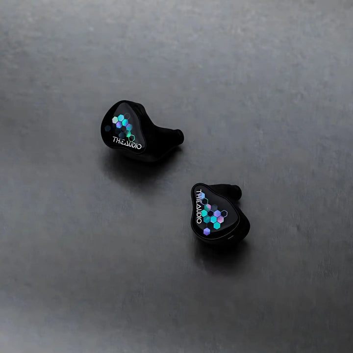 Thieaudio Monarch MKIV IEMs with Kaleidoglow faceplate sitting diagonally face up on grey background